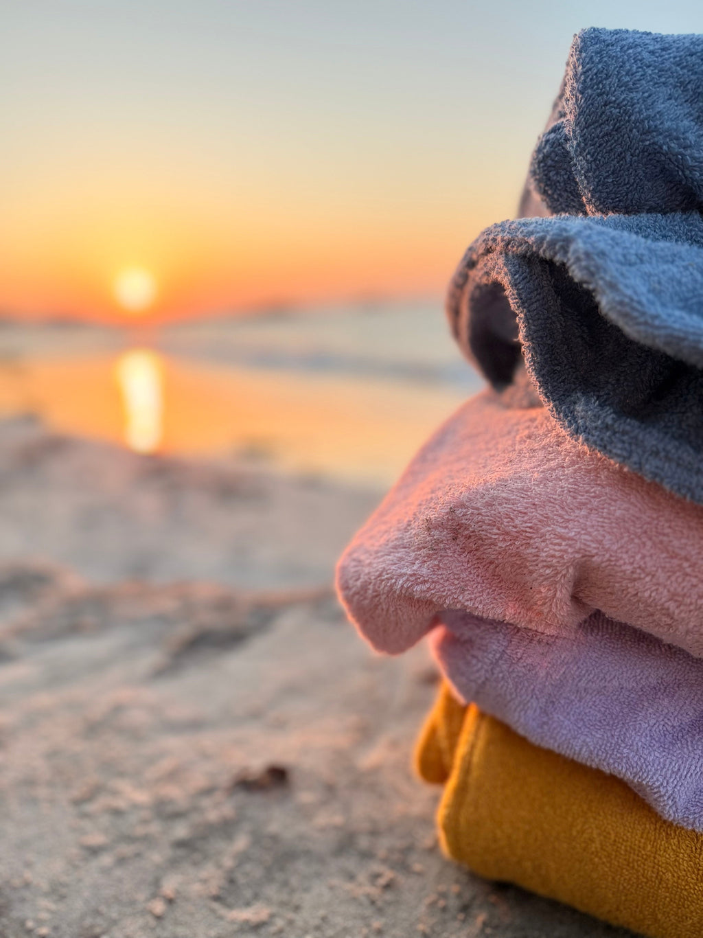 Stack of colorful towels on a sandy beach with a sunset in the background