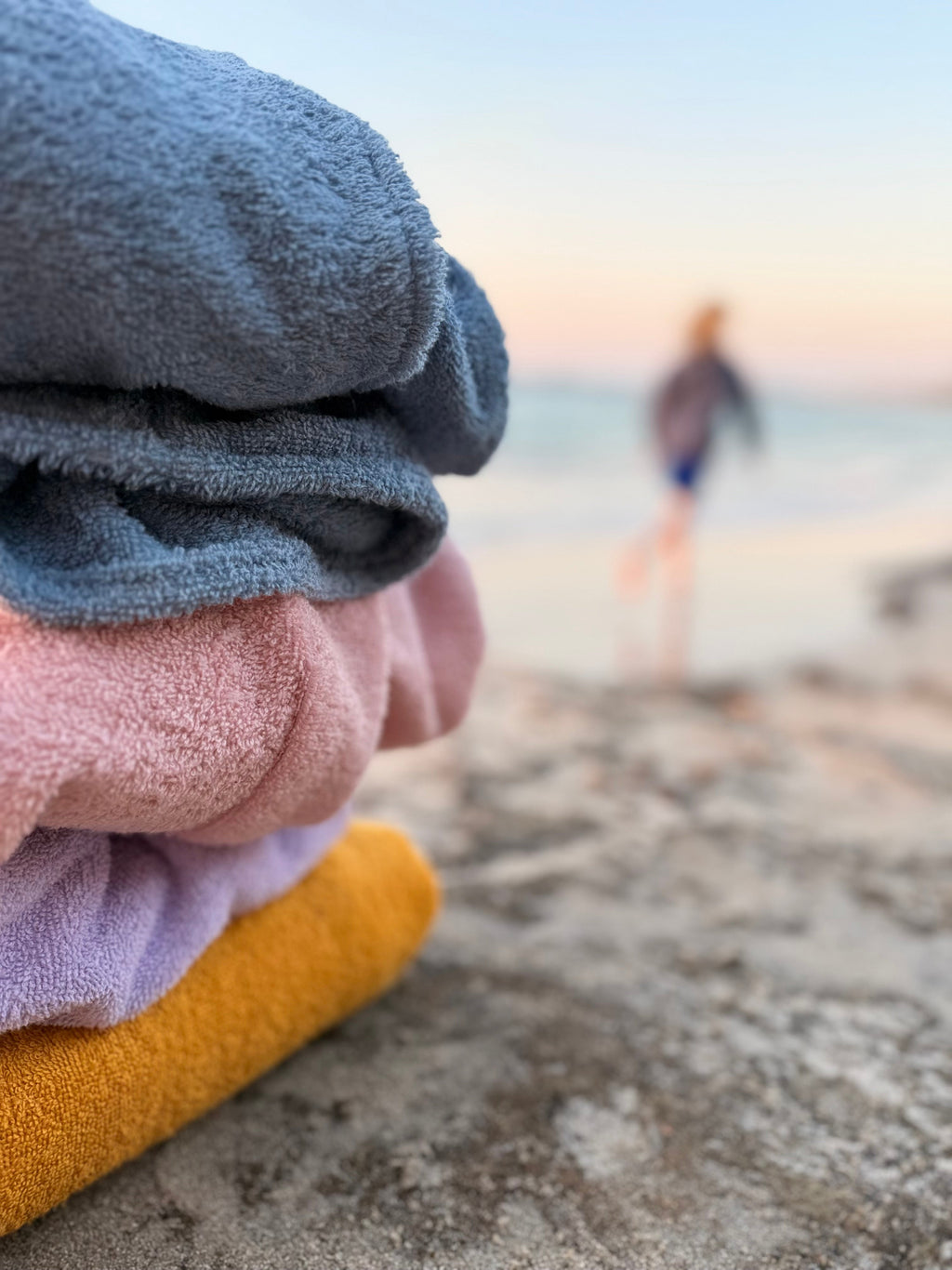 Stack of folded towels in blue, pink, and yellow on a beach with a blurred background