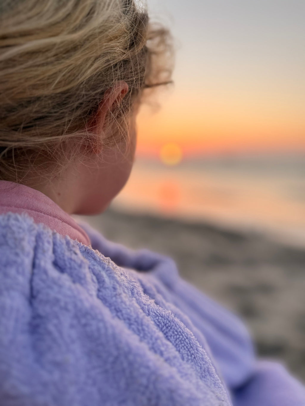 Person wrapped in a towel at sunset on a beach