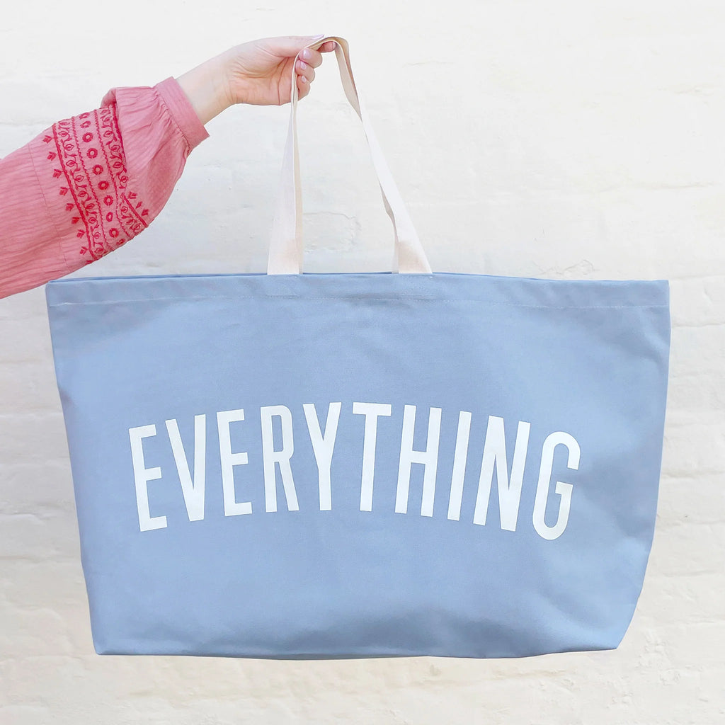 Blue tote bag with 'EVERYTHING' text held by a person wearing a pink sleeve.