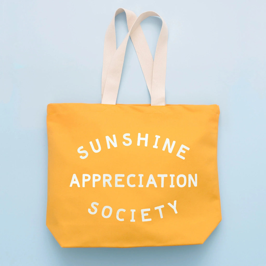 Yellow tote bag with 'Sunshine Appreciation Society' text on a light blue background