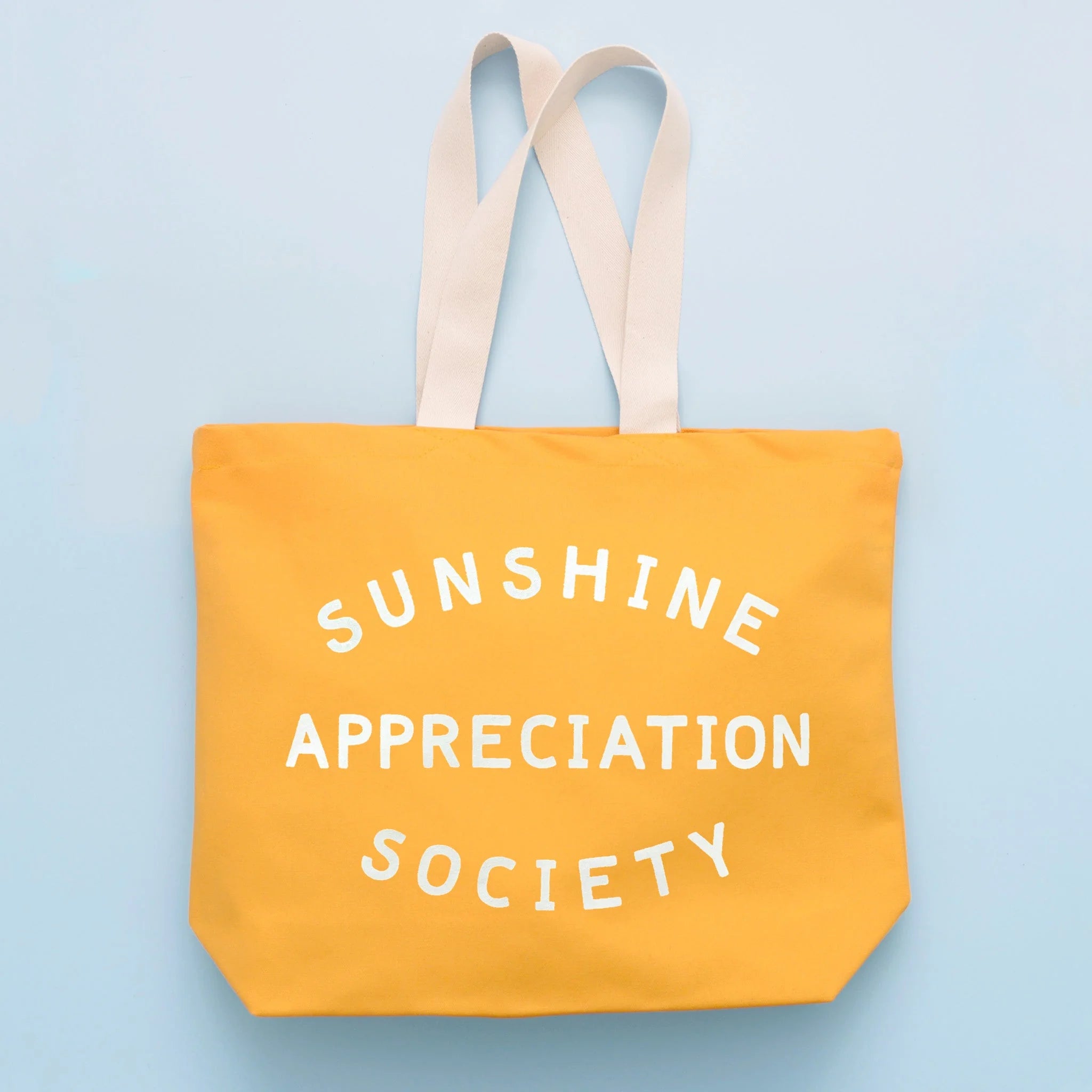 Yellow tote bag with 'Sunshine Appreciation Society' text on a light blue background